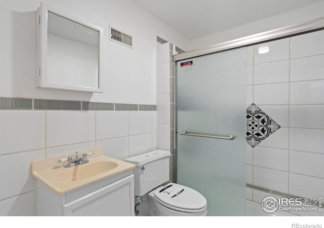 bathroom featuring a shower with door, tile walls, visible vents, toilet, and vanity