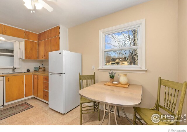 kitchen with white appliances, a sink, light countertops, backsplash, and brown cabinets