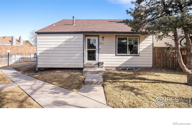 view of front facade with a front lawn, roof with shingles, and fence