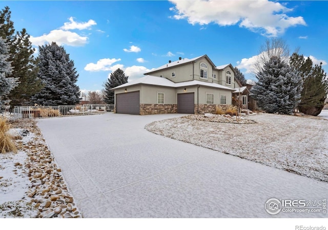 view of front of home with driveway, stone siding, an attached garage, fence, and stucco siding