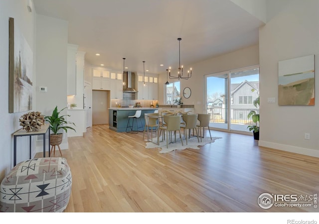 kitchen featuring pendant lighting, white cabinetry, light countertops, wall chimney exhaust hood, and an inviting chandelier