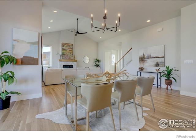 dining room with a ceiling fan, light wood-style flooring, a fireplace, high vaulted ceiling, and recessed lighting