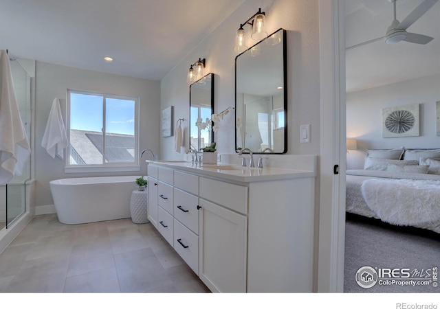ensuite bathroom featuring double vanity, a freestanding bath, ceiling fan, a sink, and ensuite bath