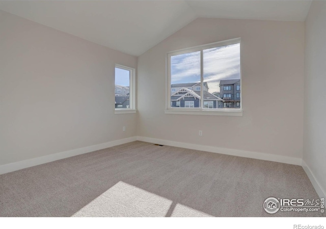 empty room featuring lofted ceiling, baseboards, visible vents, and light colored carpet