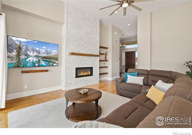 living area with a high ceiling, a fireplace, a ceiling fan, baseboards, and light wood finished floors