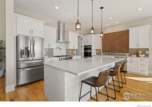 kitchen with stainless steel appliances, white cabinetry, wall chimney range hood, and a spacious island