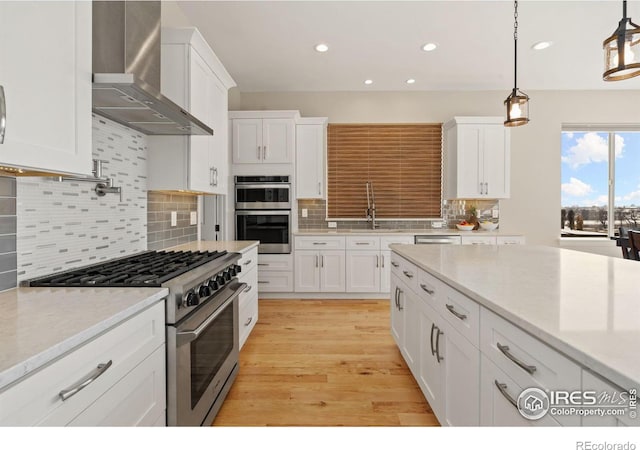 kitchen with stainless steel appliances, light wood-style floors, white cabinets, wall chimney exhaust hood, and pendant lighting