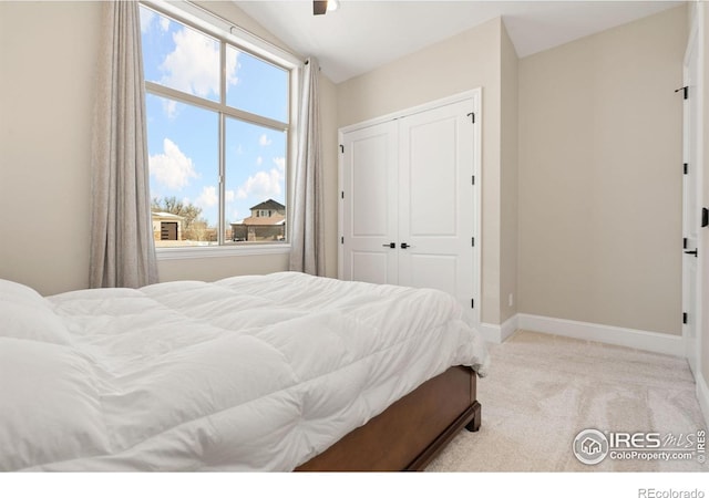 bedroom featuring light carpet, a closet, vaulted ceiling, and baseboards