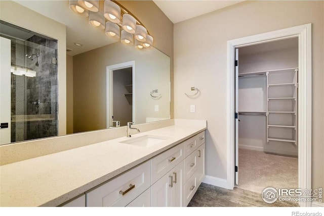 bathroom featuring a walk in closet, baseboards, a shower stall, and vanity