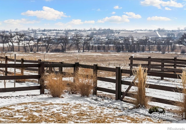 yard layered in snow with a rural view and fence