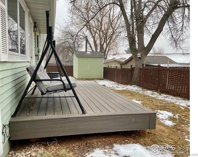 snow covered deck featuring a fenced backyard, an outdoor structure, and a storage unit