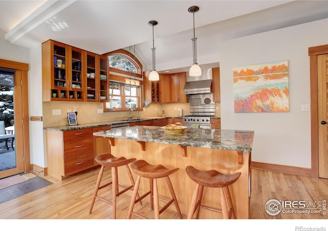 kitchen featuring decorative light fixtures, brown cabinets, glass insert cabinets, dark stone countertops, and high end stove