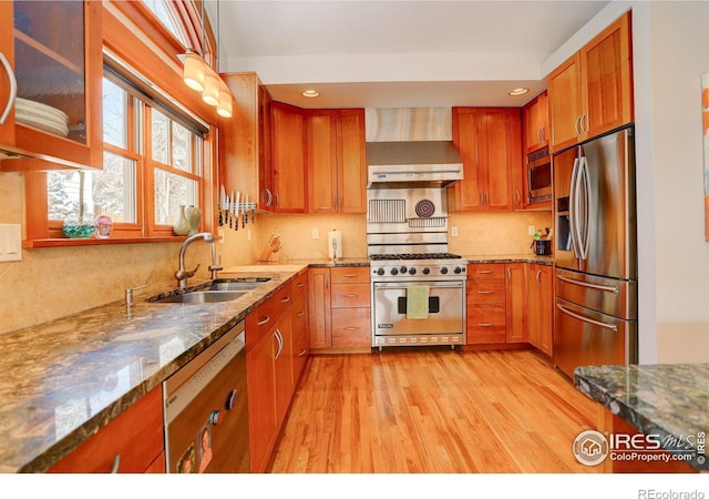 kitchen with stainless steel appliances, light wood-style flooring, a sink, wall chimney range hood, and light stone countertops