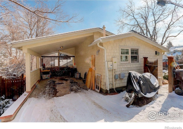 view of snow covered exterior with driveway, an attached carport, and fence