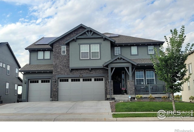 craftsman inspired home with a garage, stone siding, solar panels, and concrete driveway