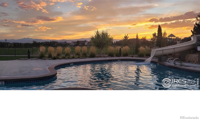 7086 Thunderview Dr, Timnath, CO 80547 - pool at dusk featuring fence, a water slide, a mountain view, and a patio