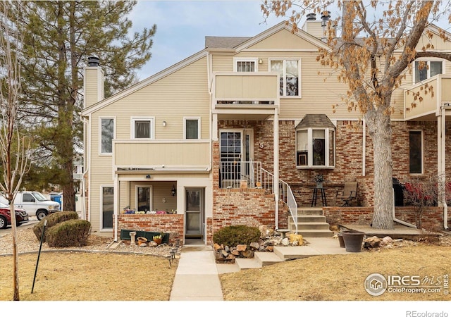 townhome / multi-family property with brick siding, a chimney, and a balcony