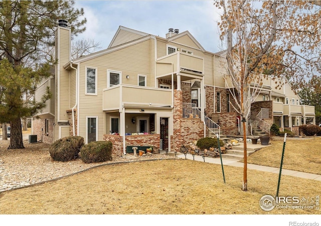 view of front of home with brick siding, a chimney, a balcony, and central air condition unit