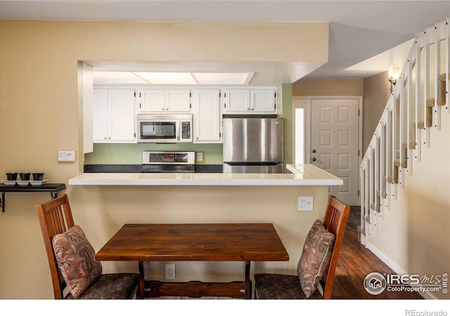 kitchen featuring dark wood-style floors, appliances with stainless steel finishes, white cabinets, a peninsula, and a kitchen bar