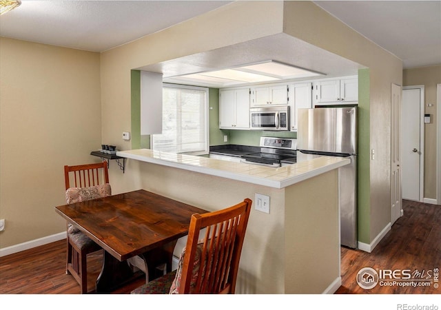 kitchen featuring appliances with stainless steel finishes, tile counters, white cabinets, and a peninsula