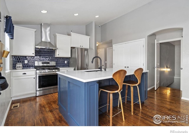 kitchen featuring a center island with sink, light countertops, appliances with stainless steel finishes, white cabinets, and wall chimney exhaust hood