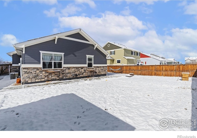 snow covered rear of property featuring central AC unit, stone siding, and fence