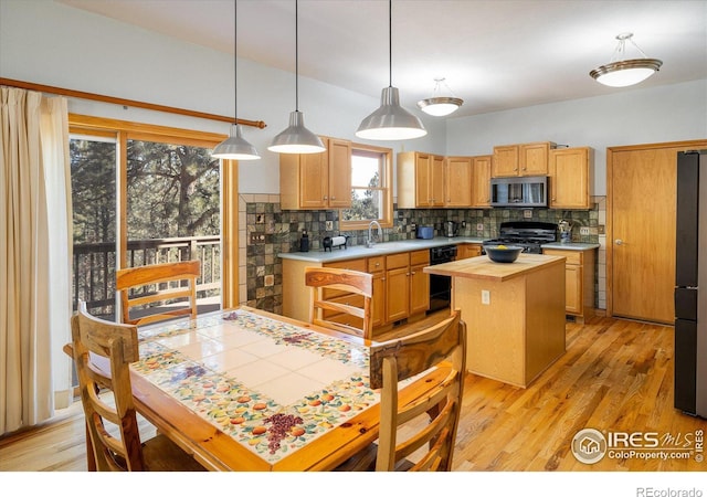 kitchen with decorative backsplash, light wood-style flooring, a center island, light countertops, and black appliances