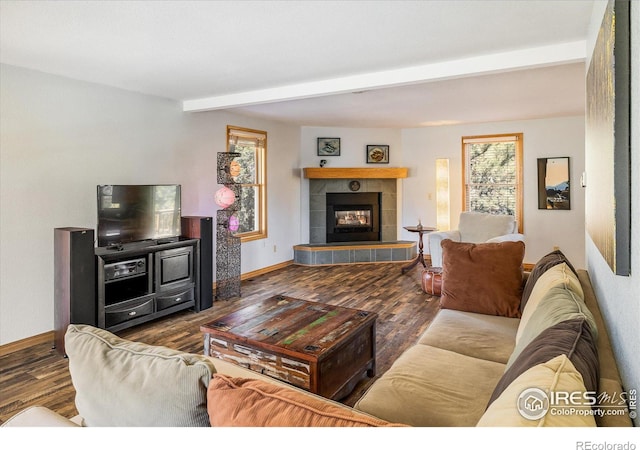 living room with baseboards, beamed ceiling, a tiled fireplace, and wood finished floors