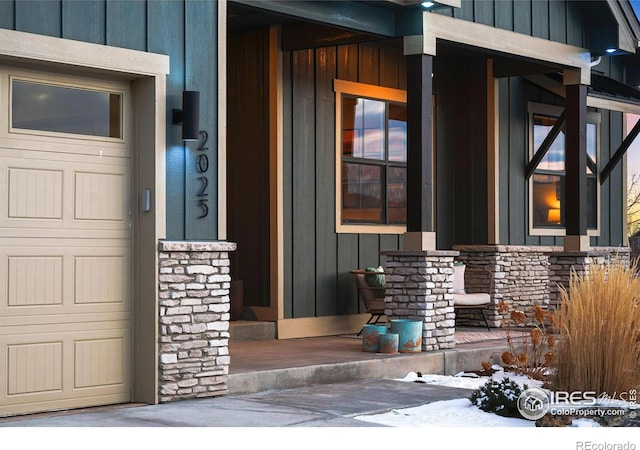 view of exterior entry with board and batten siding, stone siding, a porch, and a garage