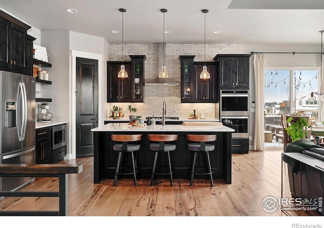 kitchen with light countertops, wall chimney exhaust hood, light wood finished floors, and stainless steel appliances