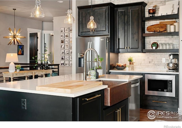 kitchen with decorative backsplash, pendant lighting, light countertops, built in microwave, and dark cabinets