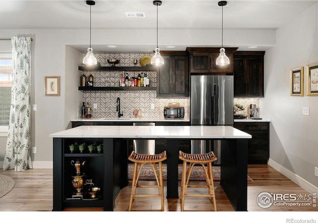 bar featuring visible vents, light wood-style floors, stainless steel fridge, a sink, and backsplash