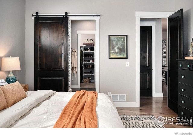 bedroom featuring a barn door, a walk in closet, wood finished floors, visible vents, and a closet