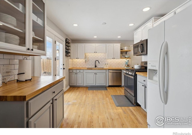 kitchen featuring stainless steel appliances, wood counters, white cabinets, light wood finished floors, and glass insert cabinets