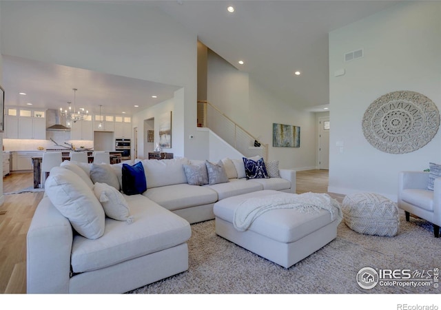 living area featuring light wood-type flooring, a towering ceiling, visible vents, and a chandelier