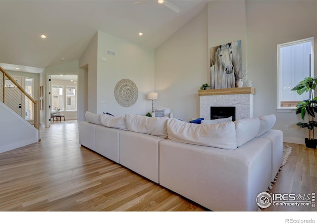 living area with high vaulted ceiling, light wood-type flooring, a fireplace, and stairway