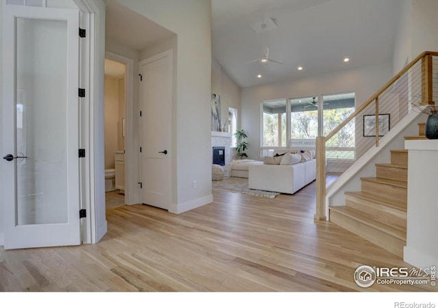 foyer entrance with recessed lighting, a ceiling fan, light wood-style floors, stairs, and a glass covered fireplace