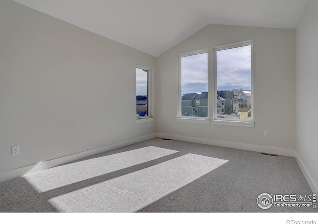 carpeted spare room featuring visible vents, vaulted ceiling, and baseboards