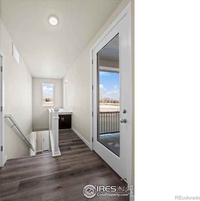 corridor with dark wood-style floors, baseboards, a textured ceiling, and an upstairs landing