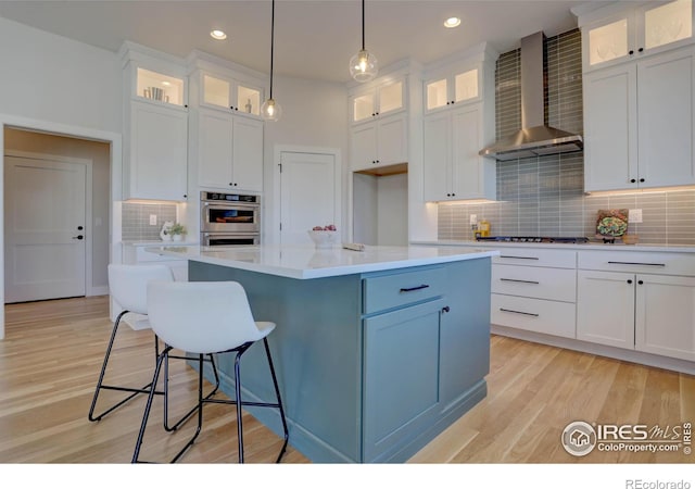 kitchen with glass insert cabinets, a center island, light countertops, and wall chimney exhaust hood