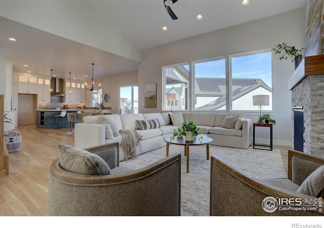 living area with light wood-style floors, recessed lighting, a stone fireplace, and ceiling fan with notable chandelier