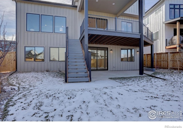 snow covered house with stairway, fence, and board and batten siding