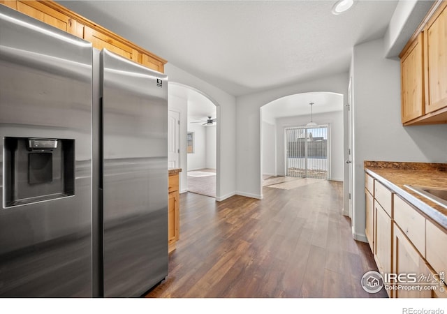 kitchen featuring arched walkways, dark wood finished floors, stainless steel fridge with ice dispenser, ceiling fan, and light brown cabinets