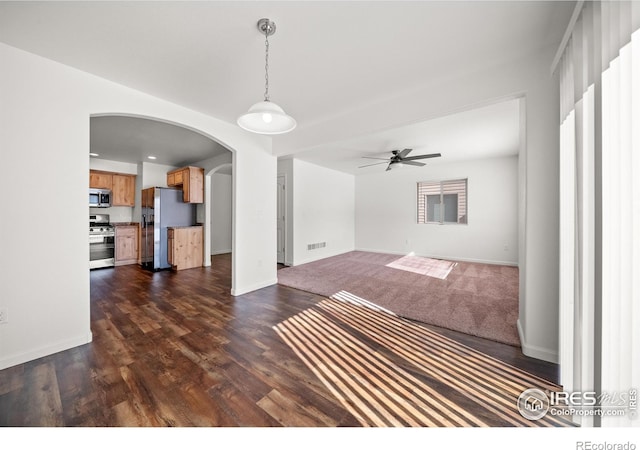 unfurnished living room with arched walkways, visible vents, baseboards, a ceiling fan, and dark wood finished floors