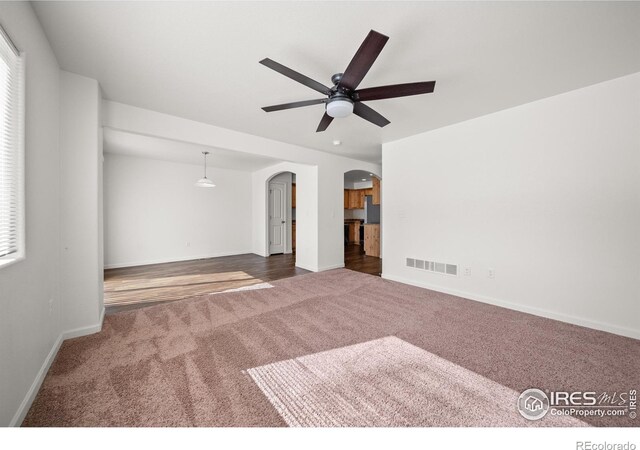 carpeted empty room with arched walkways, visible vents, ceiling fan, and baseboards