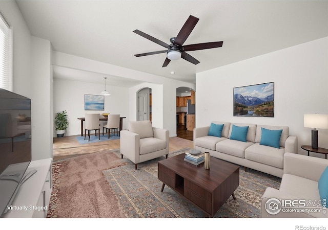 living area with arched walkways, ceiling fan, and wood finished floors