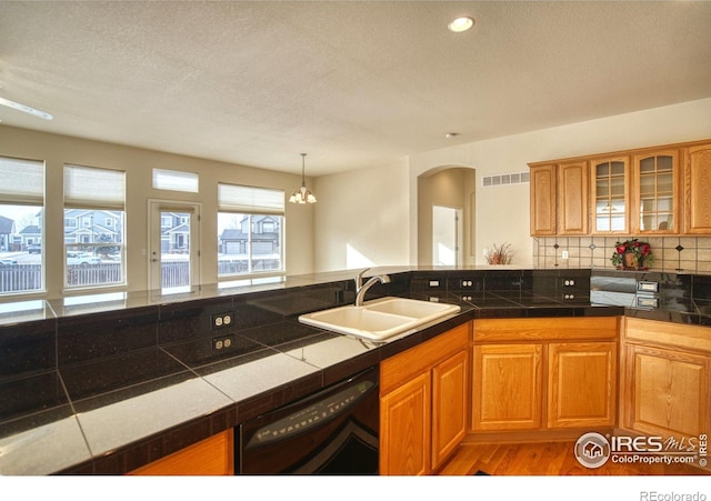 kitchen with wood finished floors, a sink, black dishwasher, tasteful backsplash, and glass insert cabinets