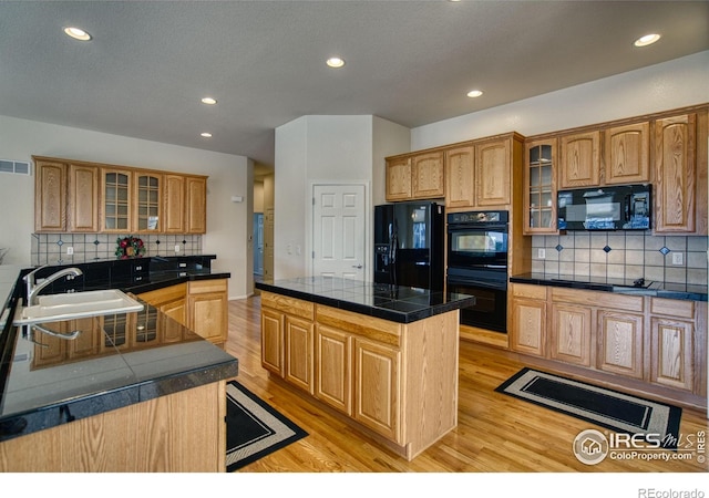 kitchen with glass insert cabinets, a sink, black appliances, and a kitchen island