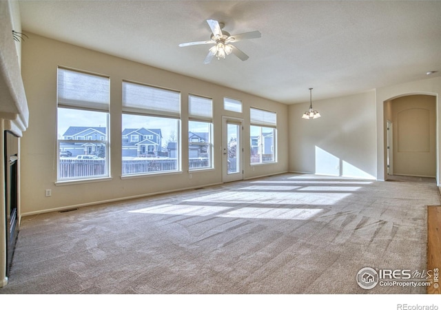 unfurnished living room with arched walkways, a textured ceiling, light colored carpet, ceiling fan with notable chandelier, and visible vents