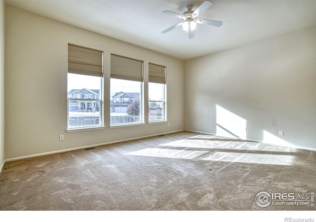 spare room featuring light carpet, ceiling fan, visible vents, and baseboards